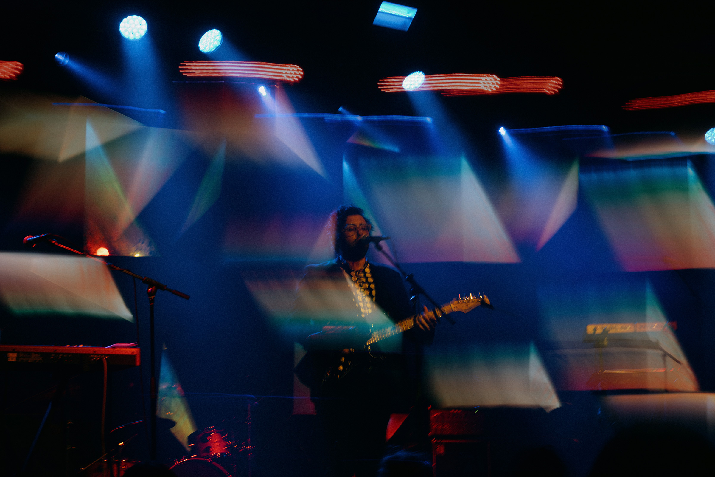 composite image of glassio at elsewhere performing a solo act with rainbow backlights streaked across the frame